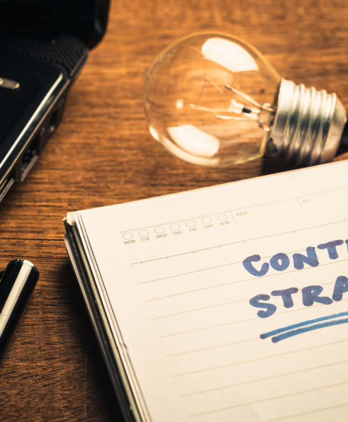 computador, caderno escrito content estrategy uma caneta e uma lâmpada acesa