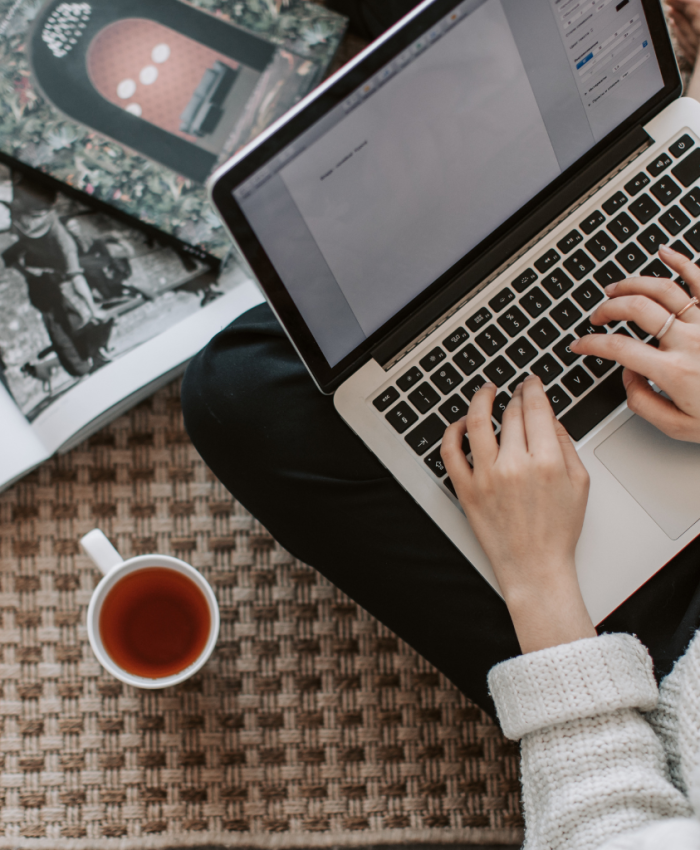 as mãos de uma pessoa aparecem digitando em um laptop o que sugere que ela está criando algo e não recorrendo ao uso de IA, ao lado uma caneca com café